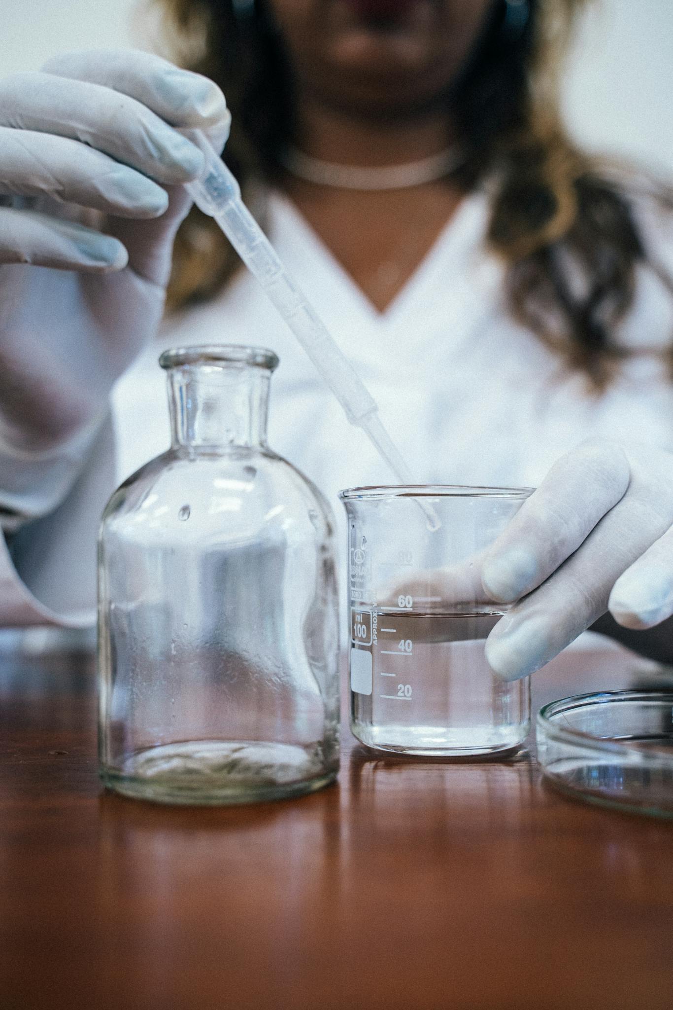 Chemist using a pipette and beakers for a laboratory experiment, wearing gloves.